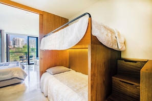 A modern bedroom with a bunk bed, wooden headboard, and a view of high-rise buildings.