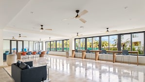 A spacious, well-lit room with large windows, ceiling fans, and a mix of seating arrangements including a sofa and chairs.