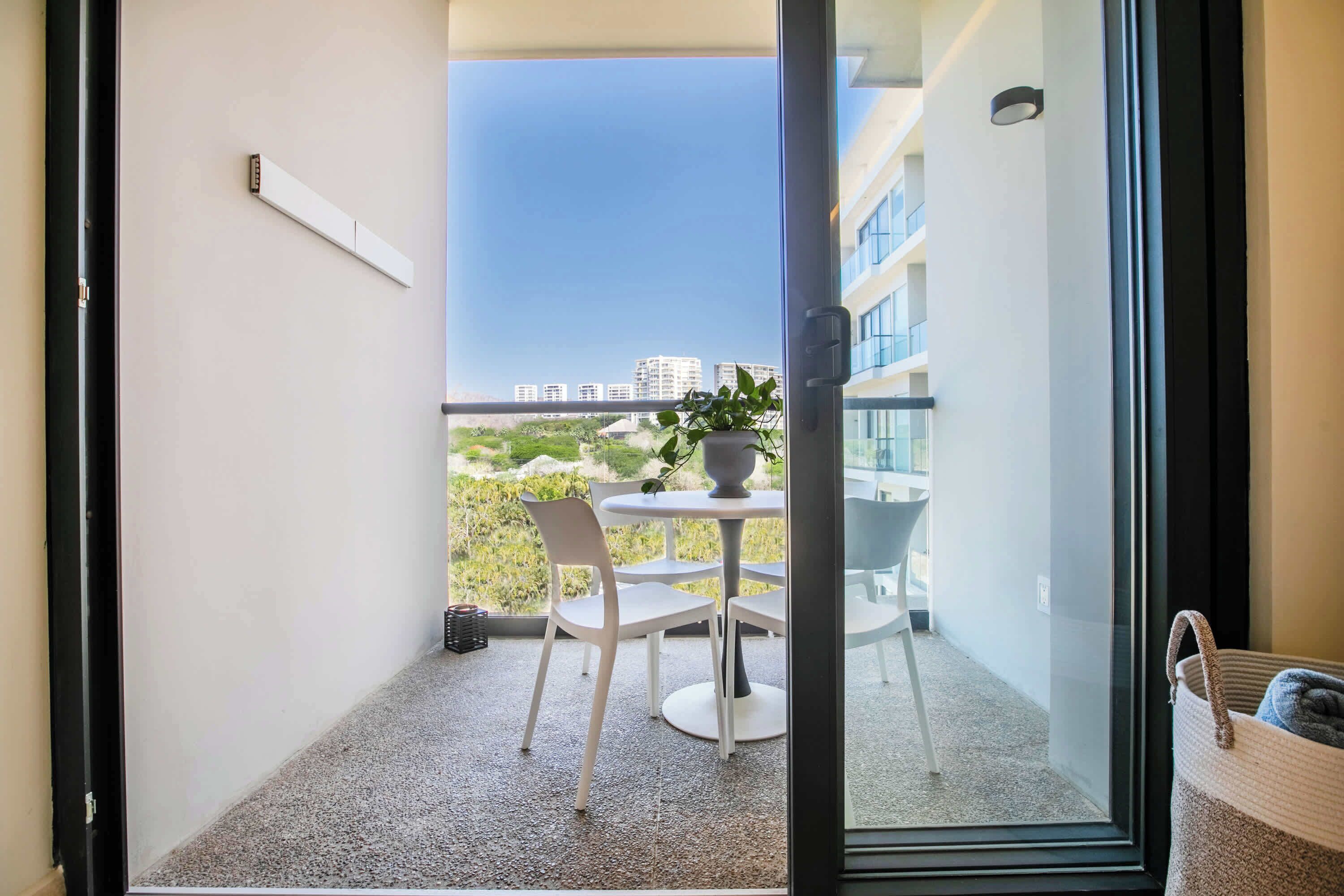 Een balkon met een tafel en stoelen, een bloempot en een uitzicht op gebouwen in de verte.