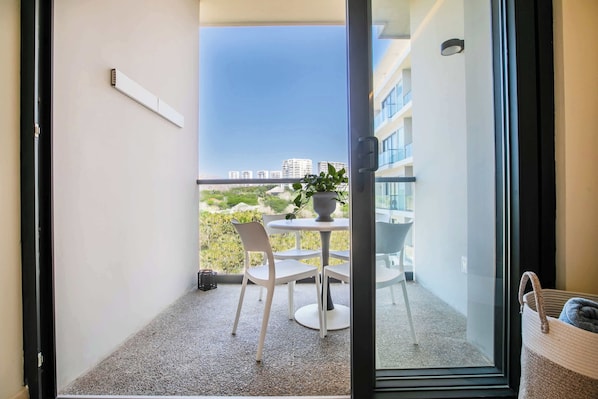 A balcony with a table and chairs, a potted plant, and a view of buildings in the distance.