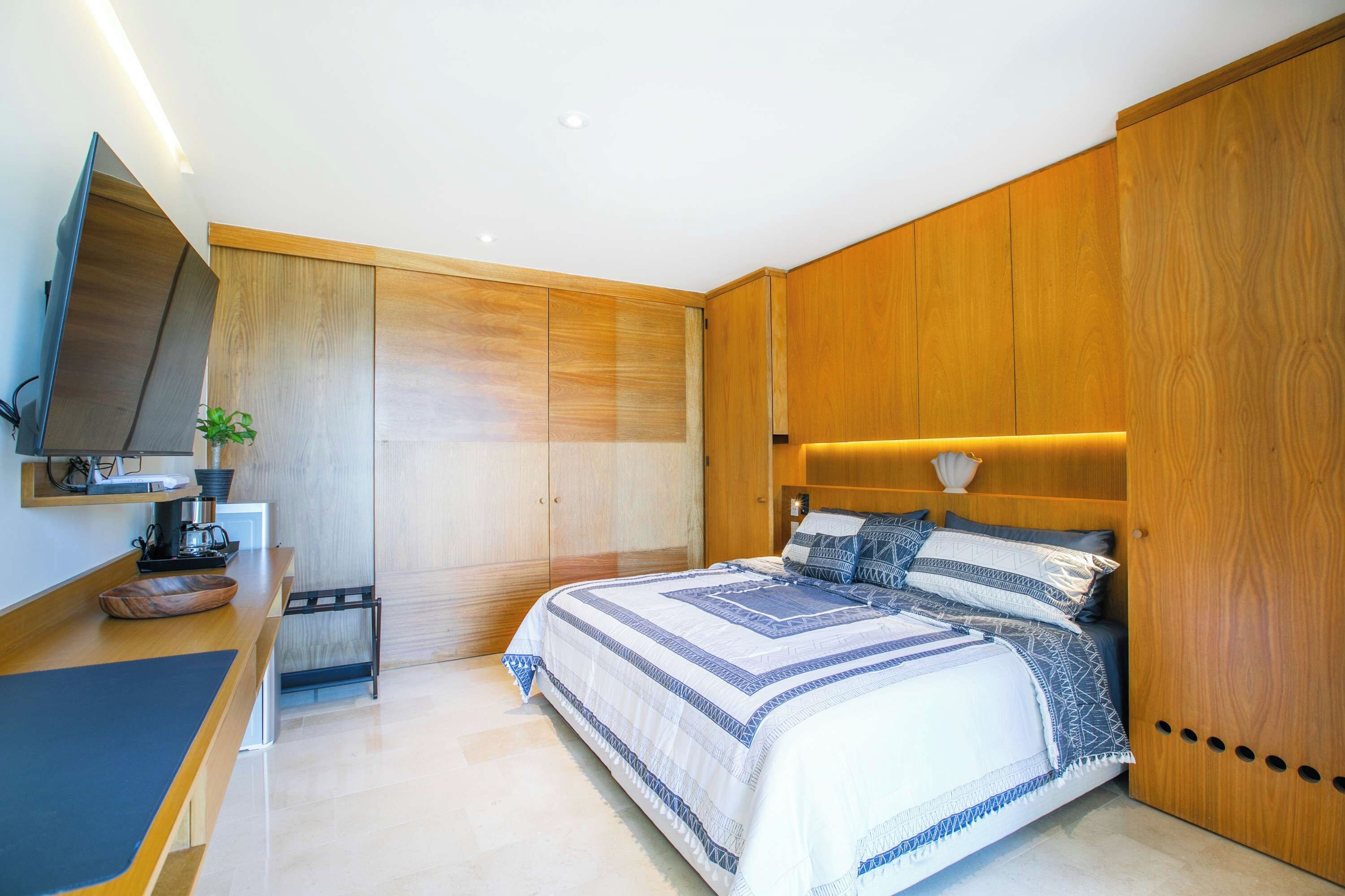 A modern bedroom with a large bed, wooden wardrobe, and a flat-screen TV.