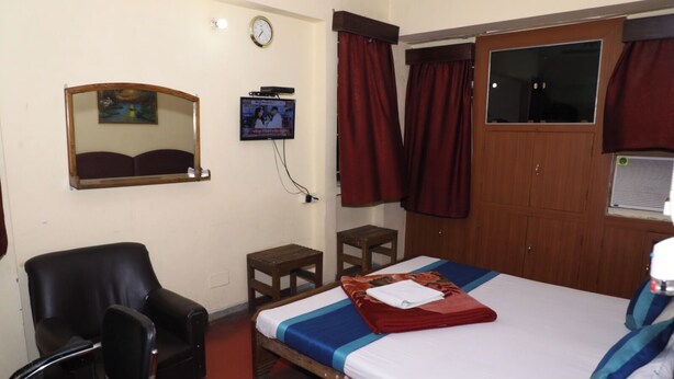 A hotel room with a bed, a chair, a small table, a television, and a wardrobe. - Hotel Laxmi Inn (Patna)