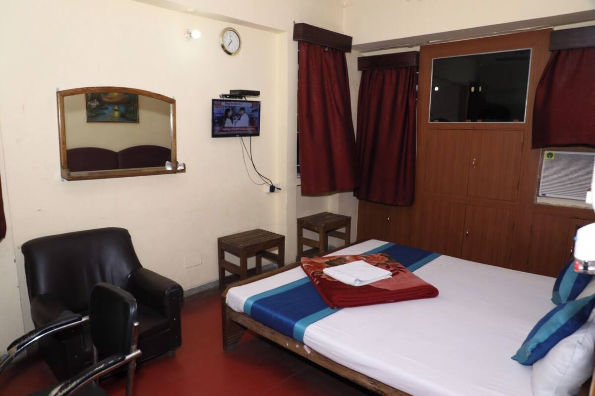 A hotel room with a bed, a chair, a small table, a television, and a wardrobe.