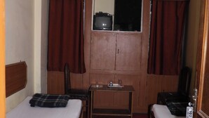 A compact hotel room with two single beds, a small table, a ceiling fan, and a window with curtains. - Hotel Laxmi Inn (Patna)
