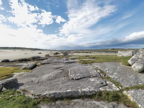 Kustlandschap met grote rotsen, grasvelden en een verre zeesterrente onder een gedeeltelijk bewolkte lucht.