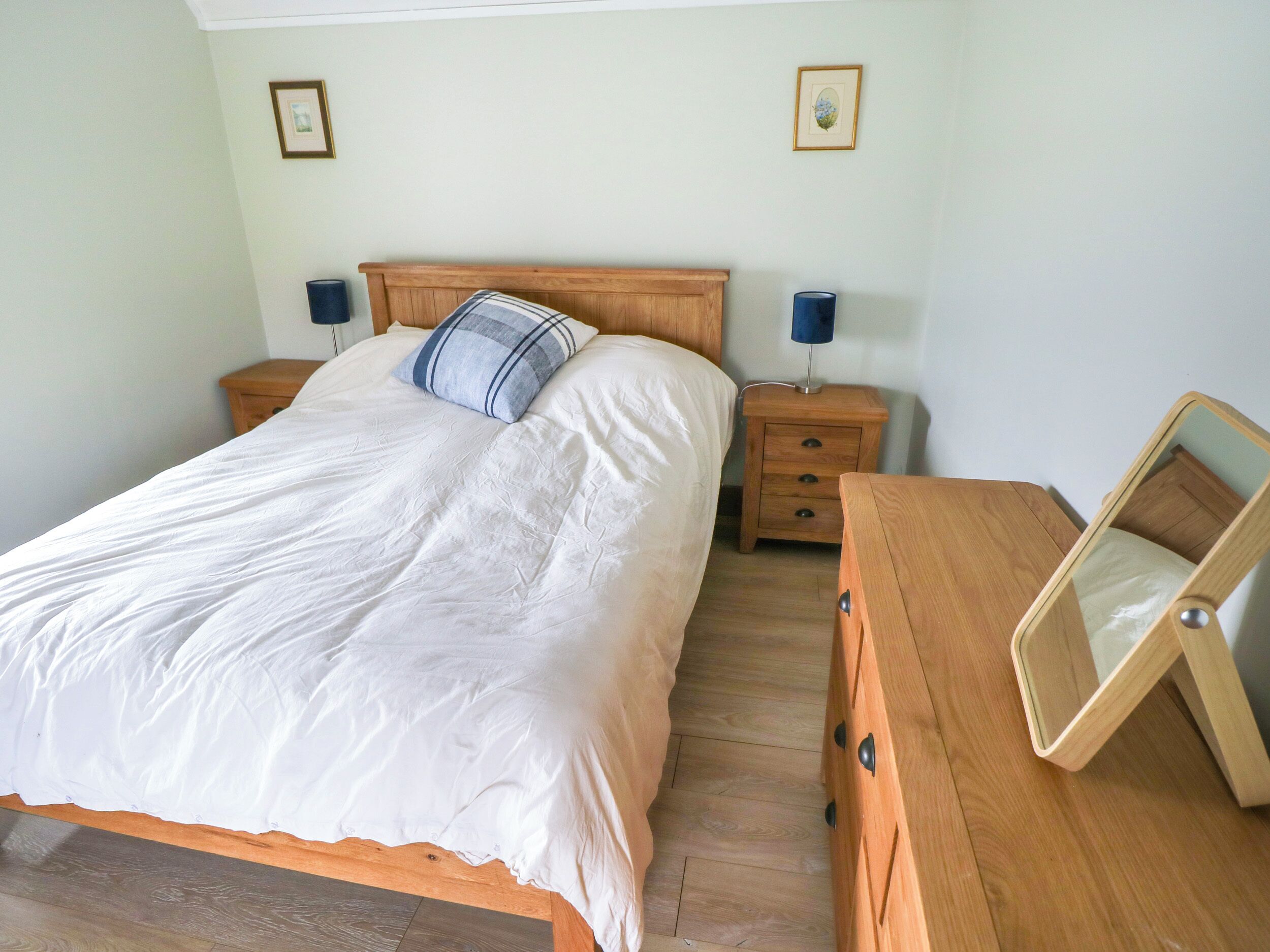 A bedroom with a wooden bed, two bedside tables, a dresser, and a mirror.