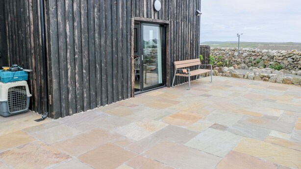 A rustic building with a wooden exterior and a stone patio. - NEAD NA BHFÁINLEOG (SWALLOWS’ NEST) in Claddaghduff, County Galway (Clifton)