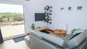 A modern living room with a grey sectional sofa, a round wooden coffee table, and a flat-screen TV mounted on the wall. - NEAD NA BHFÁINLEOG (SWALLOWS’ NEST) in Claddaghduff, County Galway (Clifton)