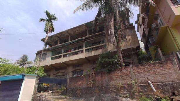A multi-story building with balconies, a brick wall, and a small structure with a blue roof. - Brahmaputra Homestay (Guwahati)