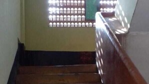 A wooden staircase with a handrail, leading to a room with a patterned window. - Brahmaputra Homestay (Guwahati)