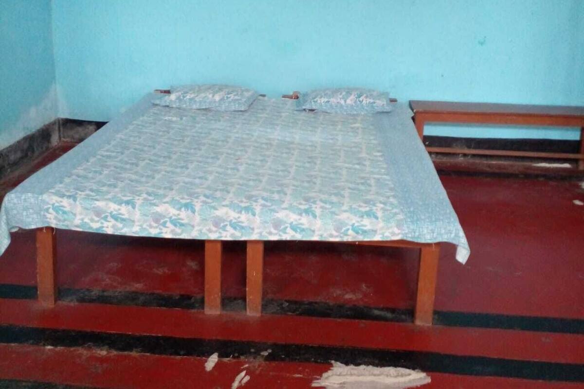 Une pièce comprenant un lit, un banc et une boîte électrique fixée au mur.