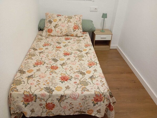 A single bed with floral bedding, a bedside table with a lamp, and a green pillow. - Tourist apartment in Simat de la Valldigna, Well equipped, 15 min from the beach (Simat de la Valldigna)