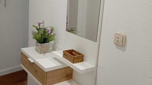Ein Badezimmer mit weißem Waschtisch, einem Spiegel und einer kleinen Pflanze.