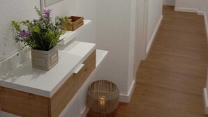 Ein Flur mit weißen Wänden, Holzboden, einem weißen Schminktisch mit Spiegel und einer kleinen Pflanze.