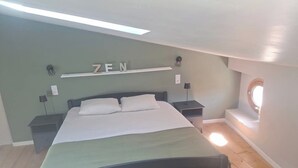 A bedroom with a bed, two nightstands, a shelf with the word "ZEN" on it, a skylight, and a circular window.