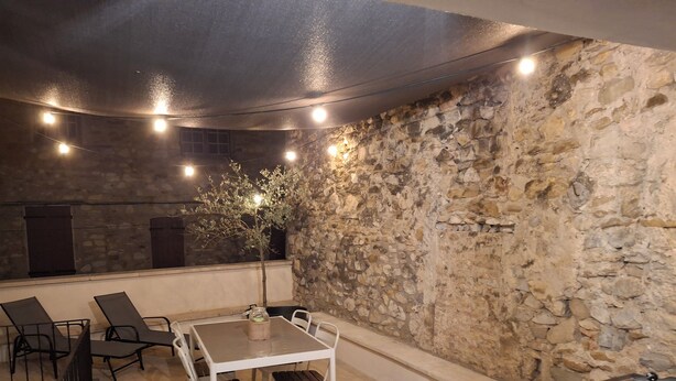 An outdoor patio with a stone wall, a table with chairs, and string lights.