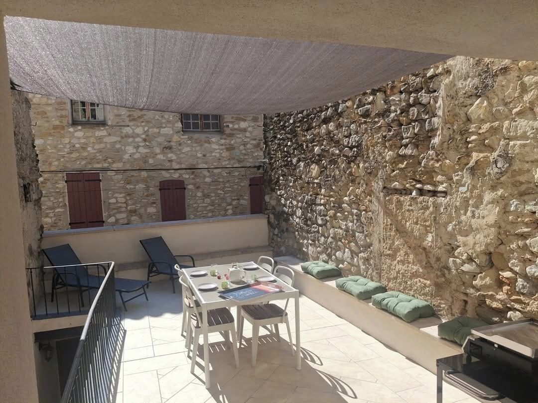 A covered outdoor patio with a stone wall, a table set for dining, and lounge chairs.