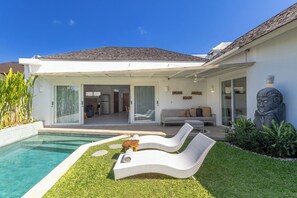 A modern house with a swimming pool, a lounge chair, and a Buddha statue.