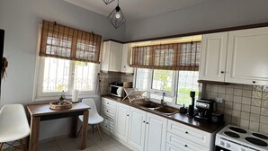 A kitchen with white cabinets, a wooden table, and a stove. - Villa Eleni Panorama Saronida (Saronida)