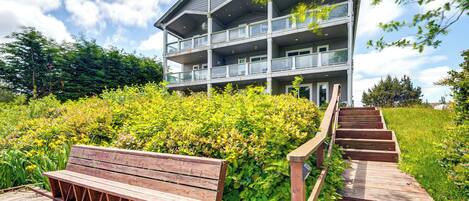 Un immeuble à plusieurs étages doté de balcons, d’un banc en bois et d’un escalier en bois menant à l’entrée.