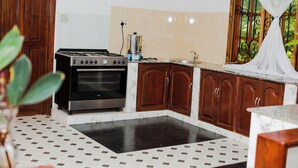 A kitchen with a stove, oven, and sink, wooden cabinets, and a tiled floor. - Kili Share Hotel & Hotel (Himo)