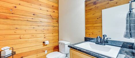 Un baño con paneles de madera, un inodoro blanco, un lavabo con espejo y una toalla colgada en la pared.