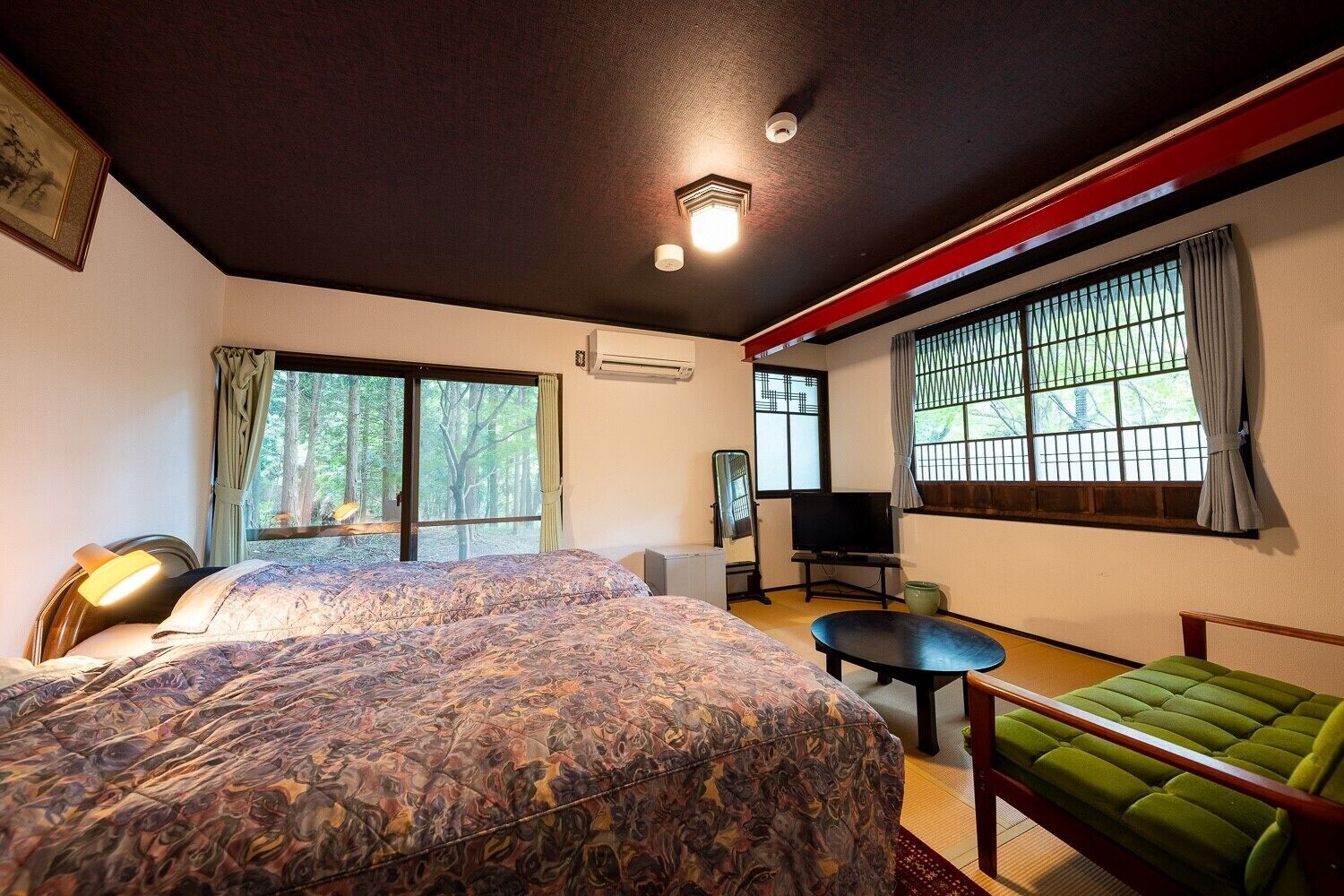 A bedroom with a bed, a TV, a green sofa, and a window with a view of trees.