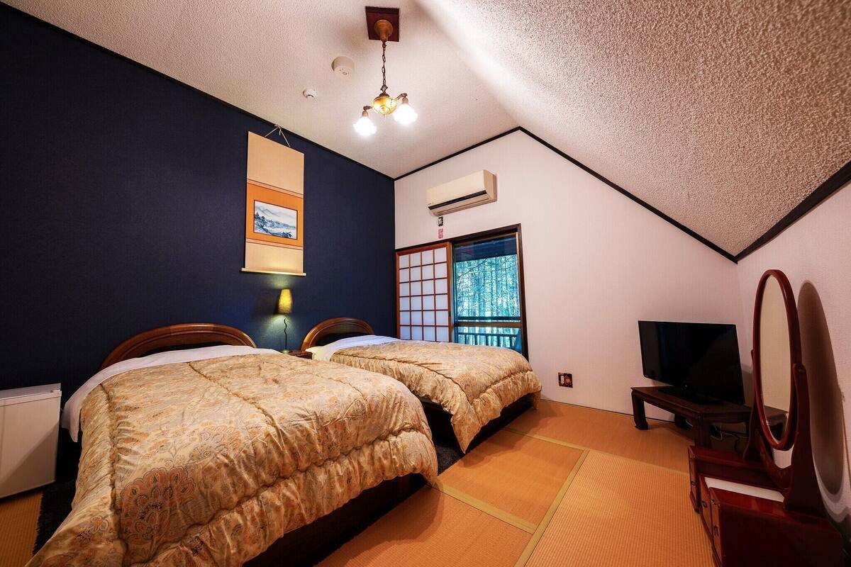 Ein Zimmer mit zwei Betten, einem Fernseher und einer traditionellen japanischen Schiebetür.