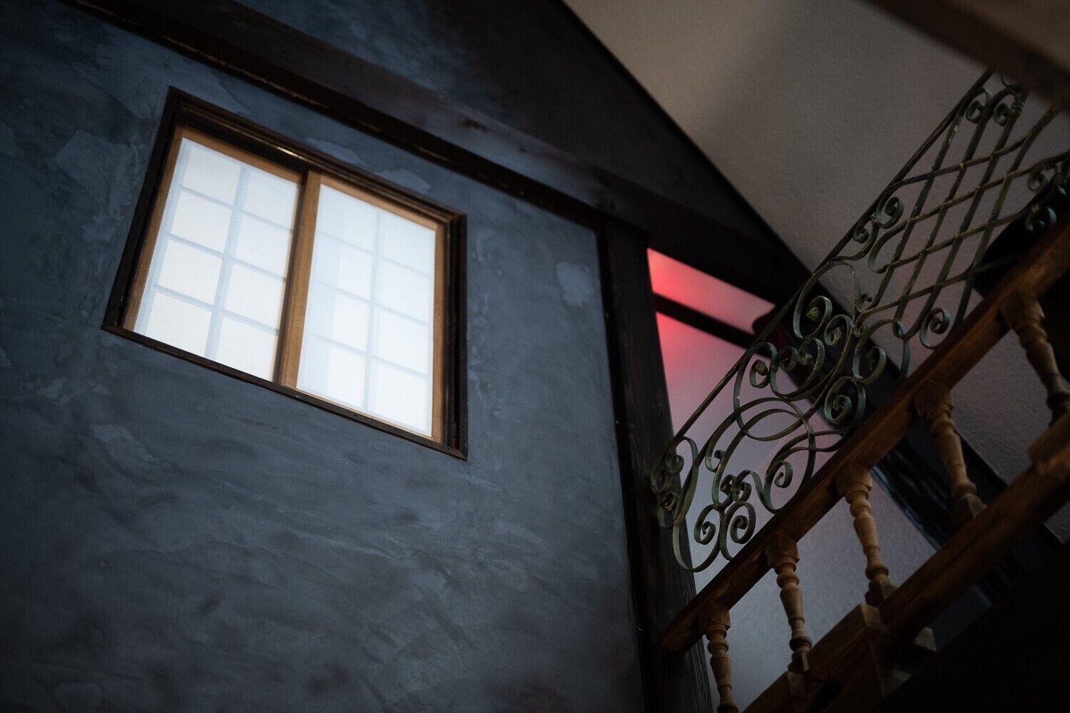 A room with a window and a staircase with ornate metal railings.