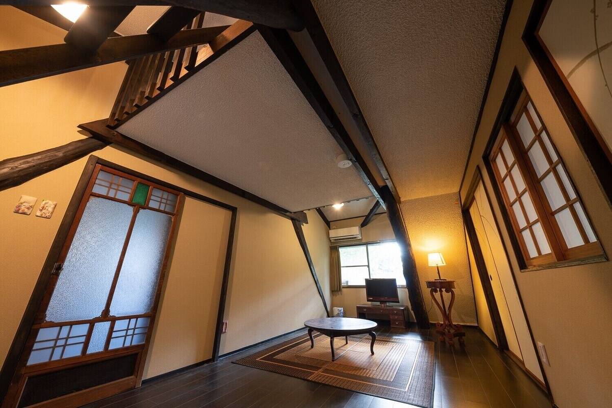 Ein traditioneller japanischer Raum mit Tatami-Boden, Schiebetüren und einer niedrigen Decke mit freiliegenden Balken.