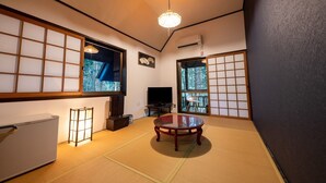 A traditional Japanese-style room with tatami flooring, a low table, a television, and sliding doors leading to a view of trees. - Taisho Yufunohana (Yufu)