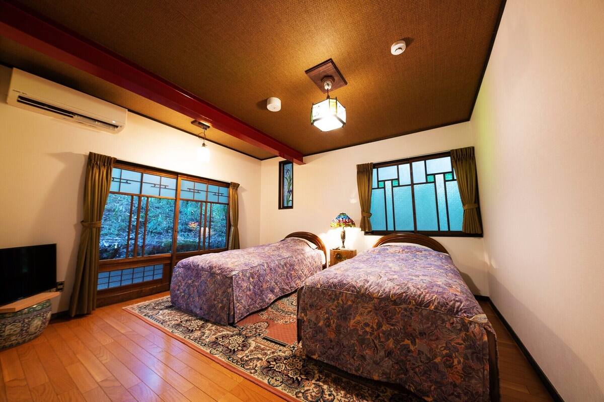 Ein Zimmer mit zwei Betten, einem Fernseher und großen Fenstern.