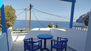 A balcony with a table and chairs, overlooking a coastal view with the sea and a rocky landscape. - Διαμέρισμα 1 Υπνοδωματίου (Καμάρι)