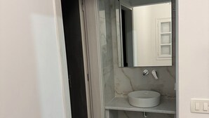 A bathroom with a white sink, a mirror, and a marble backsplash. - Διαμέρισμα 1 Υπνοδωματίου (Καμάρι)
