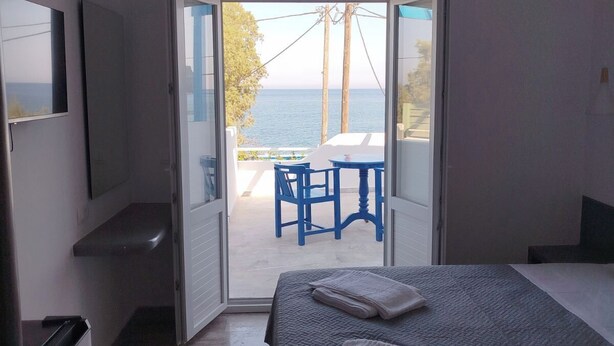 A bedroom with a bed, a TV, and an open door leading to a balcony with a table and chairs. - Διαμέρισμα 1 Υπνοδωματίου (Καμάρι)