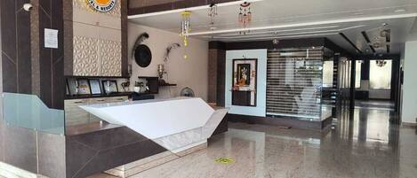 A modern hotel lobby with a reception desk, a large mirror, and a decorative wall with a citrus-themed sign.