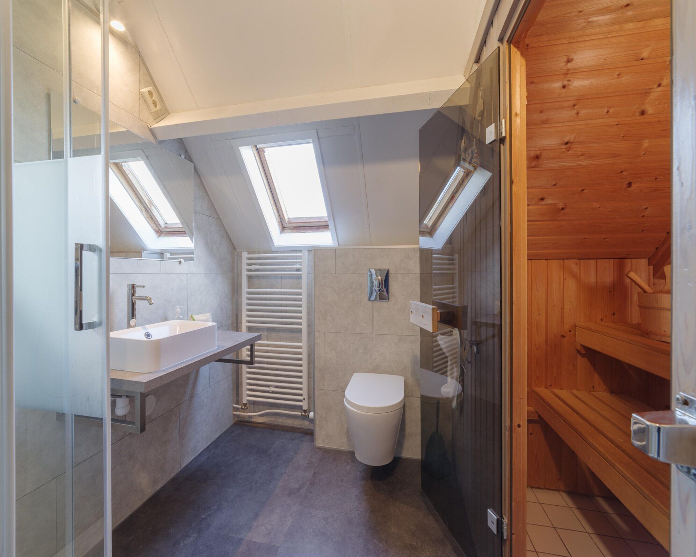 Ein modernes Badezimmer mit Oberlichtern, Toilette, Waschbecken und Duschbereich.