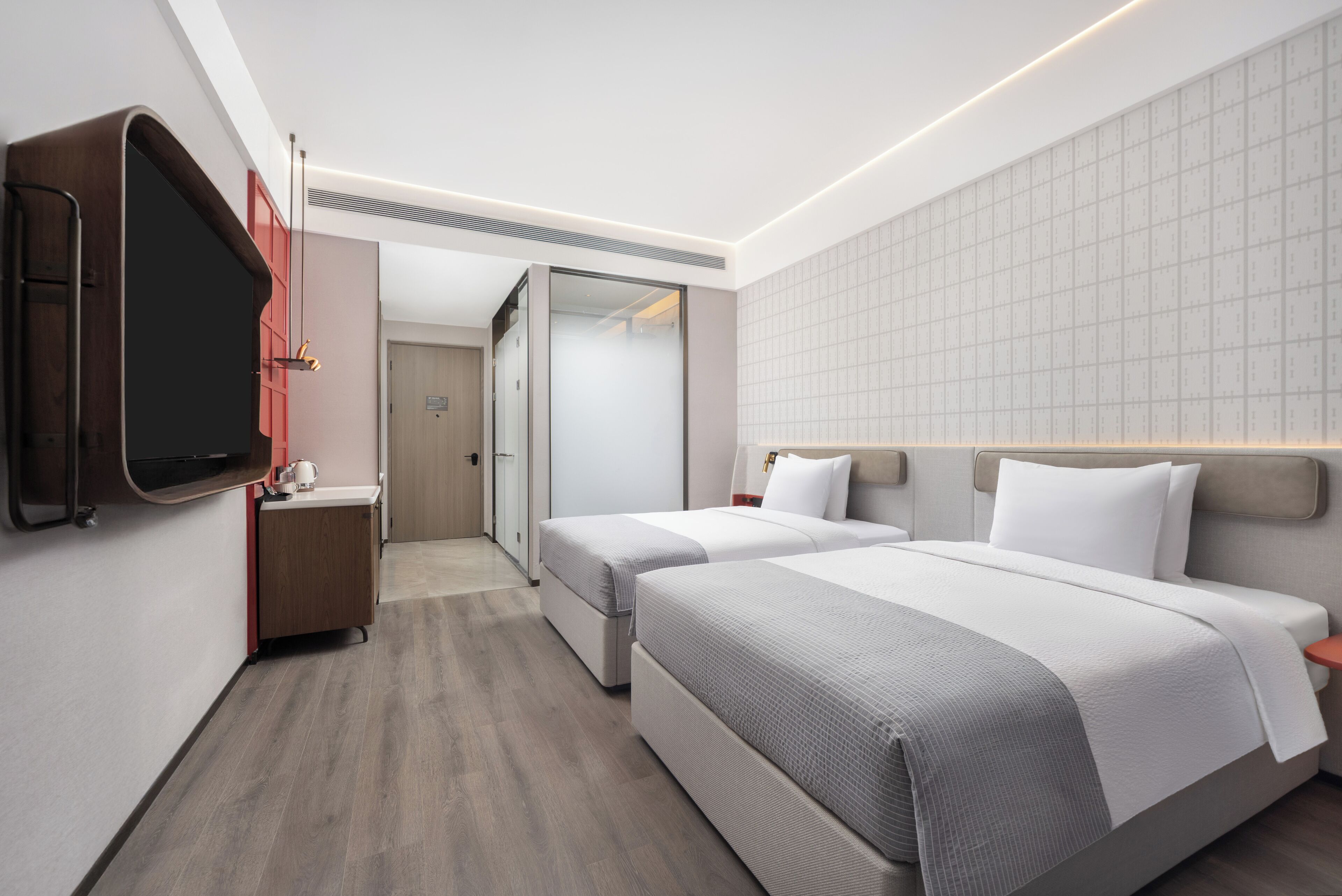 Una habitación de hotel moderna con dos camas, un televisor en la pared, un escritorio pequeño y un armario.