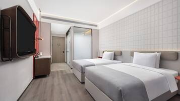 Una habitación de hotel moderna con dos camas, un televisor en la pared, un escritorio pequeño y un armario.
