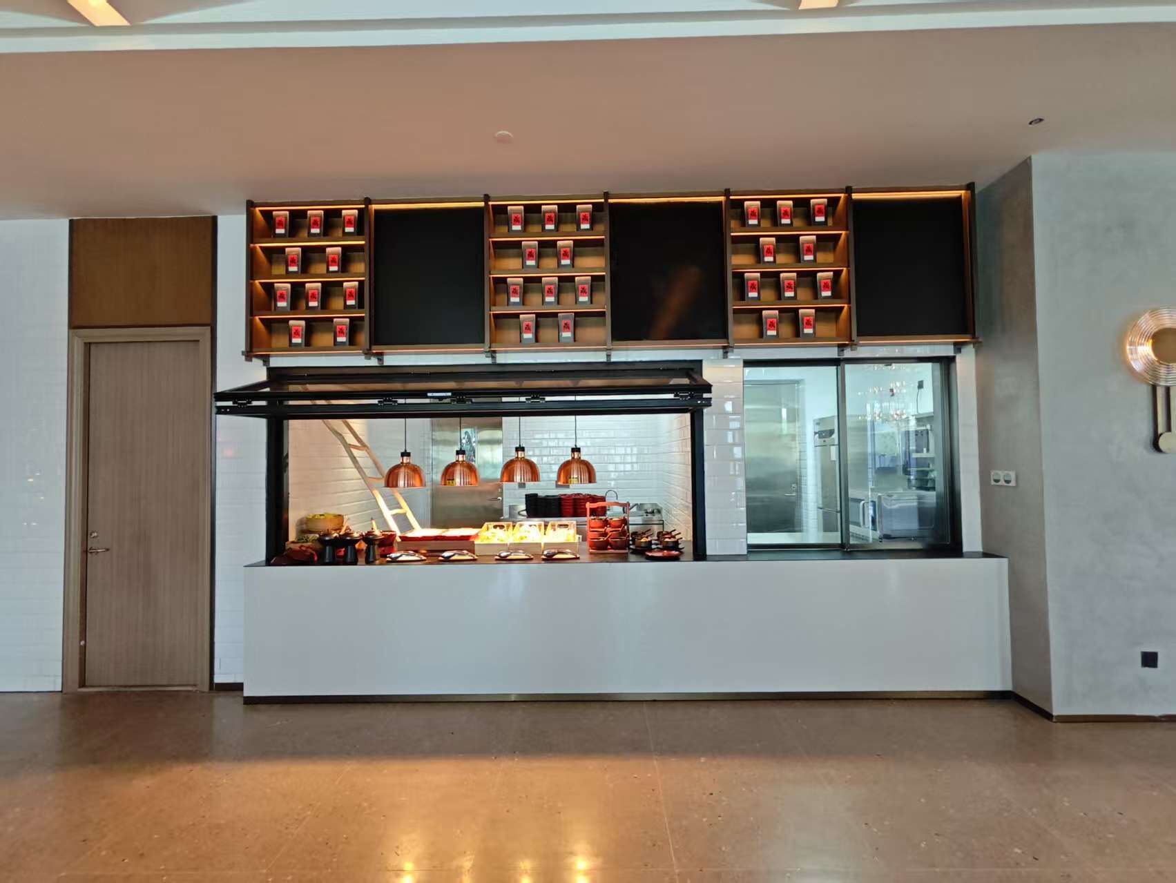 Un moderno puesto de comida con una vitrina de vidrio, estantes superiores con productos envasados e iluminación colgante de cobre.