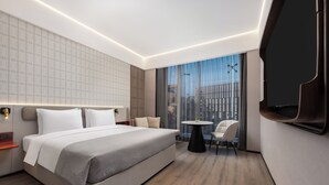 Ein modernes Hotelzimmer mit einem großen Bett, einem kleinen runden Tisch, einer Couch und einem an der Wand befestigten Fernseher.