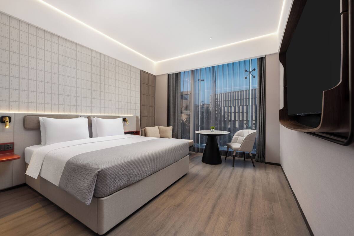 Une chambre d’hôtel moderne avec un grand lit, une petite table ronde, un canapé et un téléviseur fixé au mur.