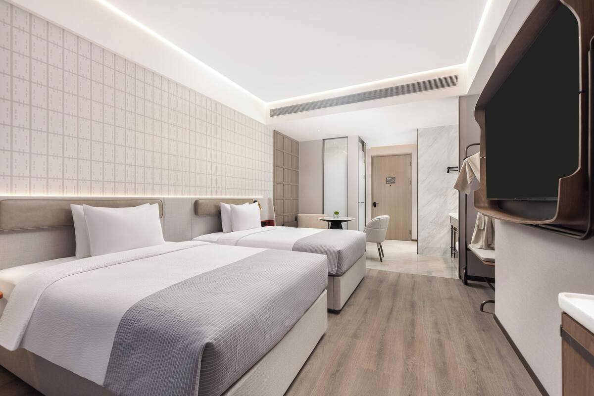 Une chambre d’hôtel moderne avec deux lits, une petite table, une chaise et un téléviseur fixé au mur.
