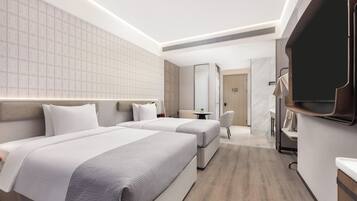 Une chambre d’hôtel moderne avec deux lits, une petite table, une chaise et un téléviseur fixé au mur.