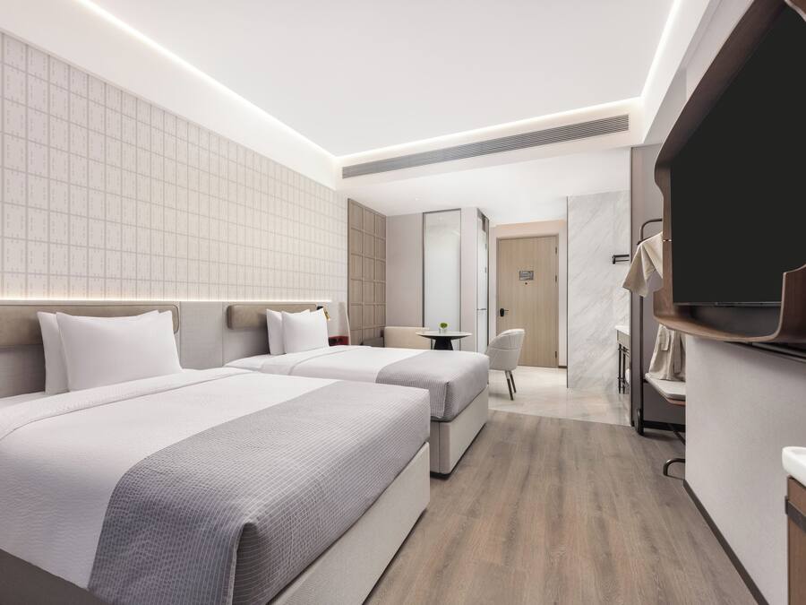 Une chambre d’hôtel moderne avec deux lits, une petite table, une chaise et un téléviseur fixé au mur.