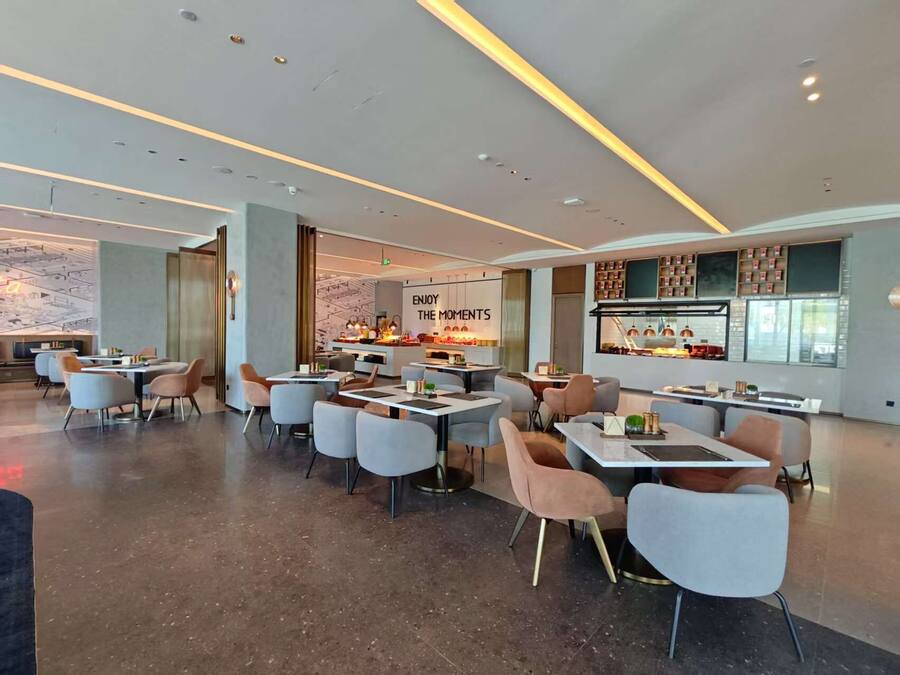 A modern restaurant with multiple seating areas, a central bar, and a wall with 'ENJOY THE MOMENTS' signage.