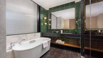 A modern bathroom with a freestanding bathtub, a large mirror, and a green-tiled wall.