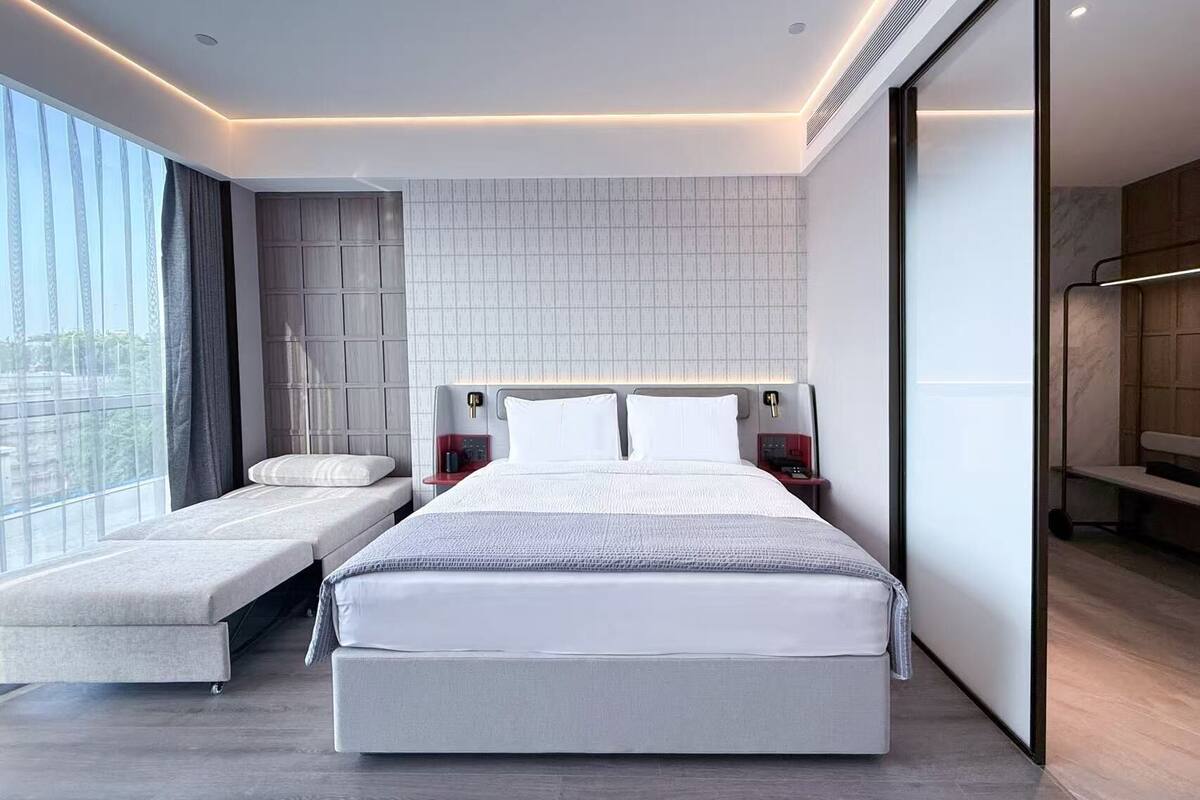 Une chambre moderne avec un grand lit, des tables de chevet, un banc et une vue sur la ville.