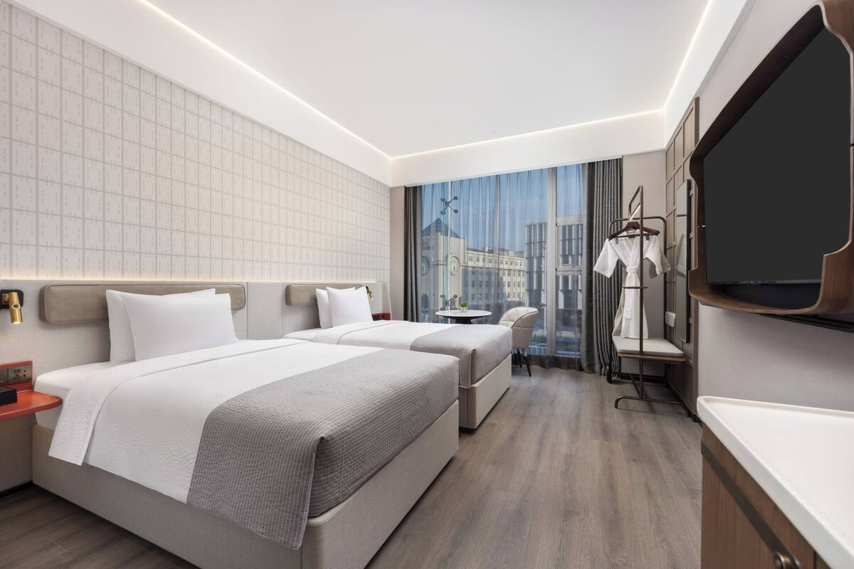 Une chambre d’hôtel moderne avec deux lits, une grande fenêtre donnant sur la ville, un téléviseur à écran plat et une petite table.