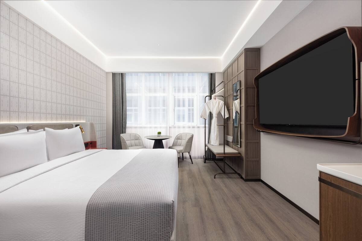 Une chambre d’hôtel moderne avec un grand lit, une petite table, deux chaises, un miroir et un téléviseur.